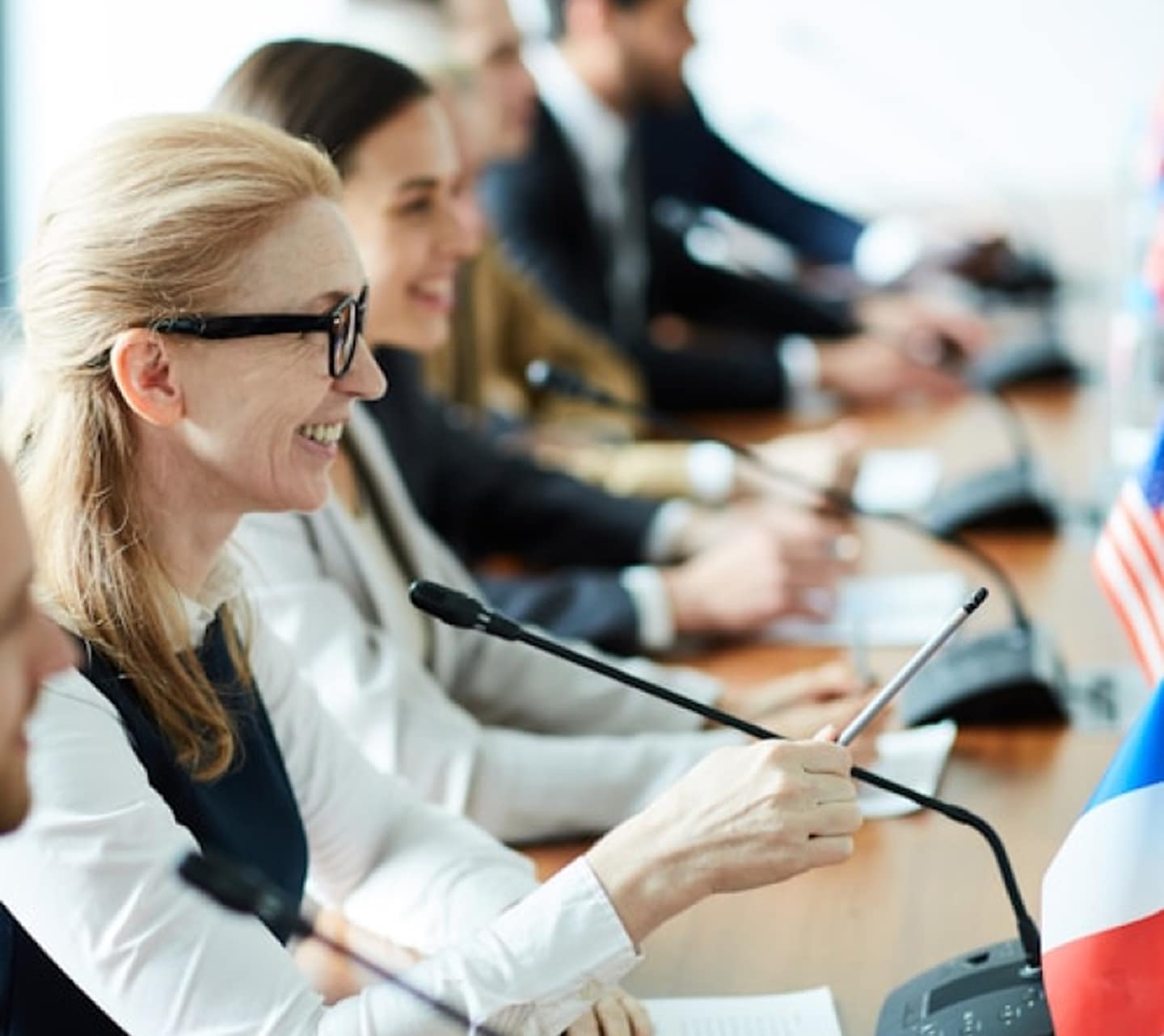 Happy confident delegate pointing with pencil while speaking in microhpone to one of colleagues making speech