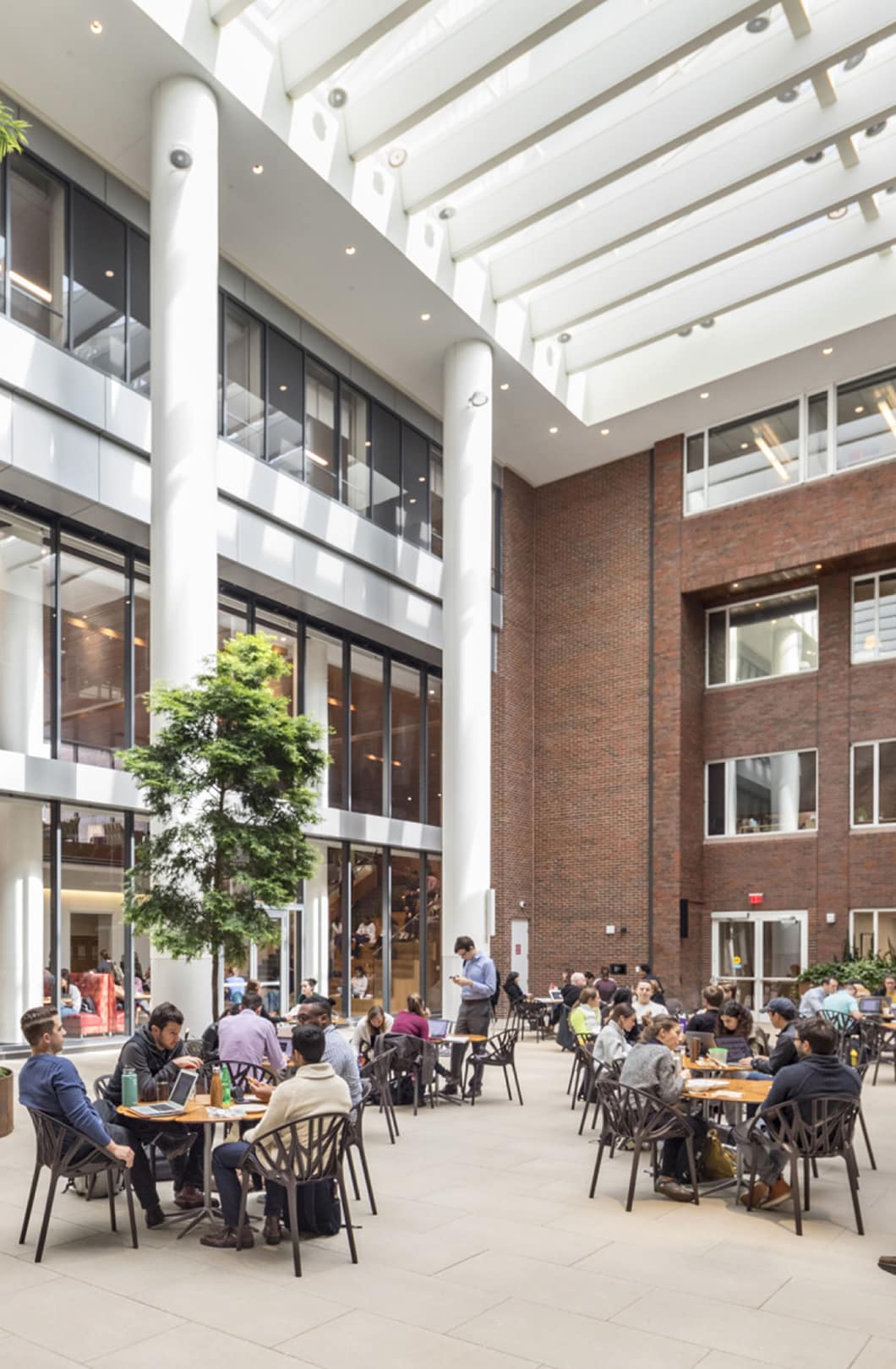 Interior of harvard Kennedy School, an inner courtyard with a glass roof and students sitting at tables.