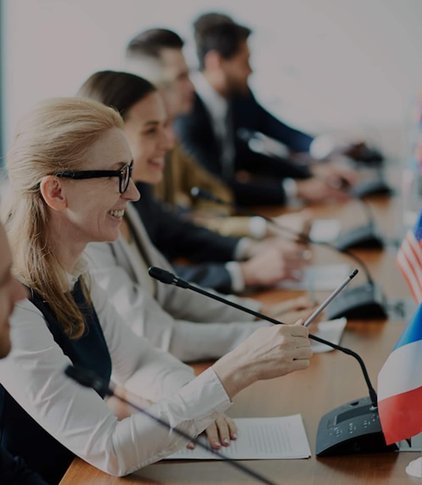 Happy confident delegate pointing with pencil while speaking in microhpone to one of colleagues making speech